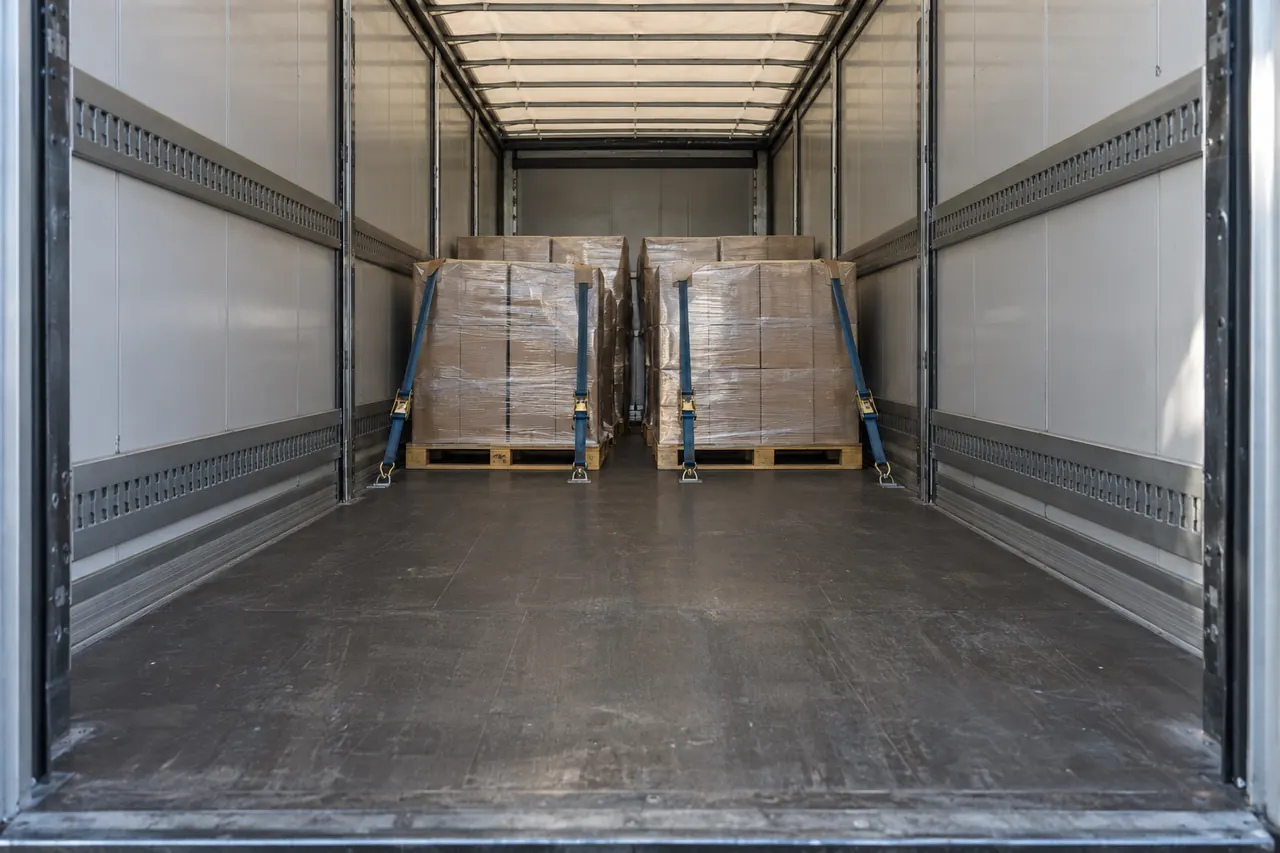 Palets bien trincados dentro de un tráiler a medio cargar, con la luz entrando por las puertas abiertas.